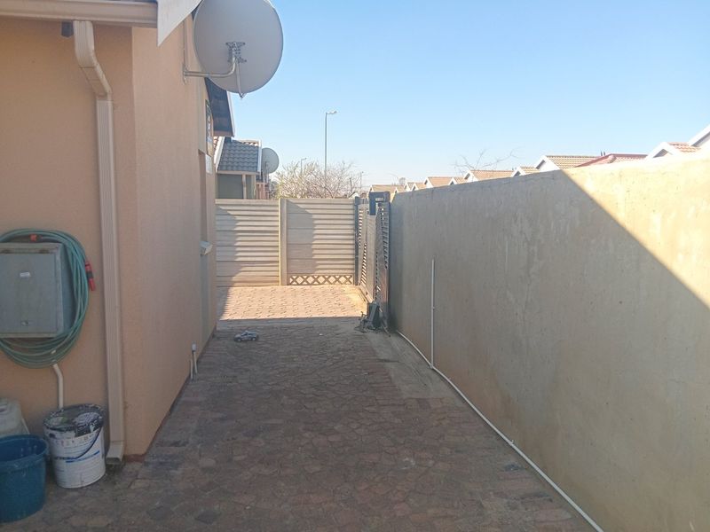 A side access path featuring paved flooring, a boundary wall, and a metal gate leading to the rear of the property.