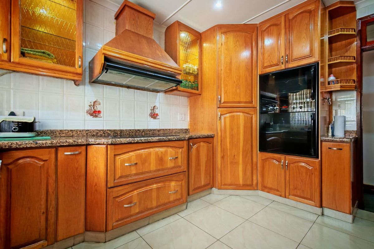 A functional kitchen featuring traditional wooden cabinetry, granite countertops, a built-in oven, and an extractor fan with tiled flooring and backsplash.