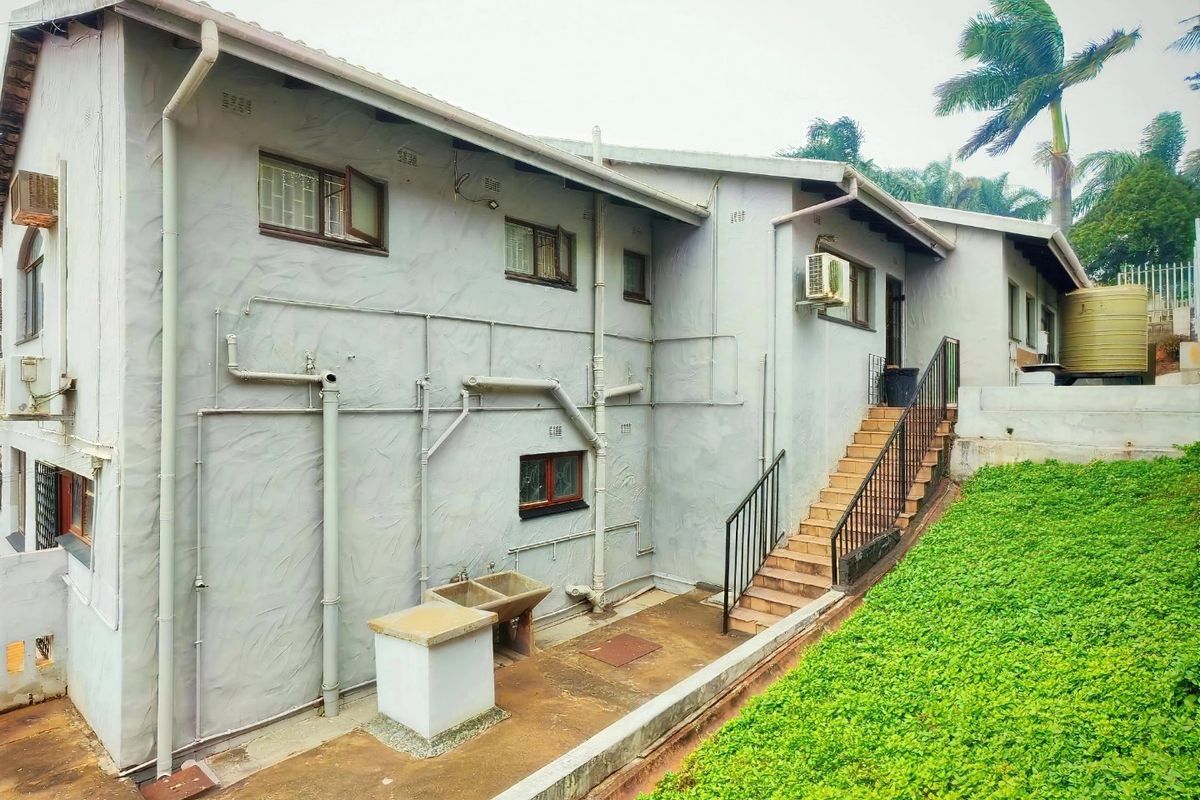 Rear exterior view of the house featuring an external staircase, concrete wash basin, and exposed utility plumbing along the side wall.