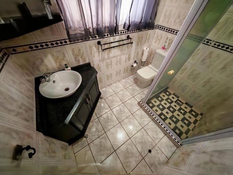 A functional bathroom featuring a corner vanity with vessel sink, a glass-enclosed shower, and tiled finishes throughout.