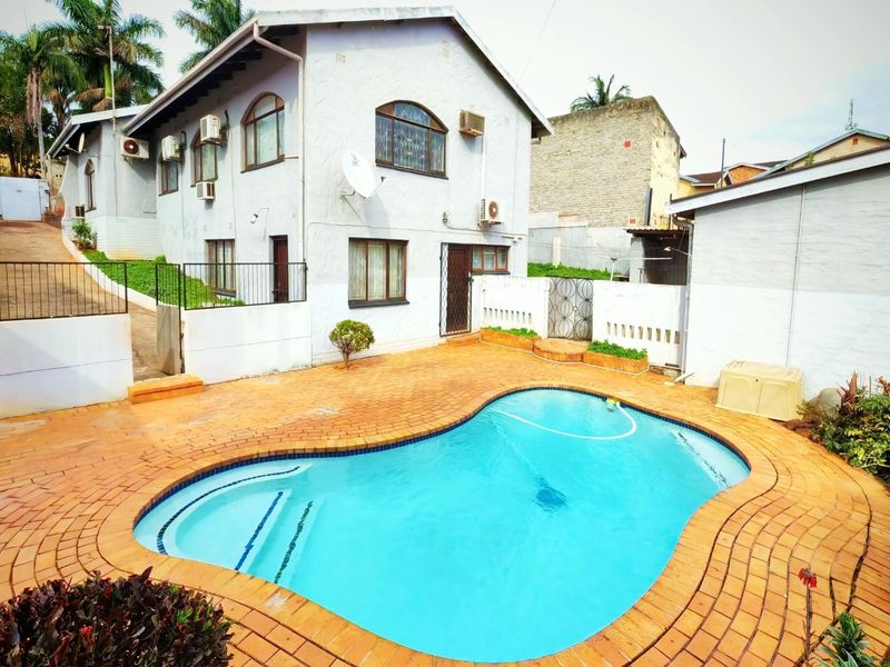 Rear exterior view featuring a swimming pool with brick paved surround, set against the side elevation of the house with multiple air conditioning units.
