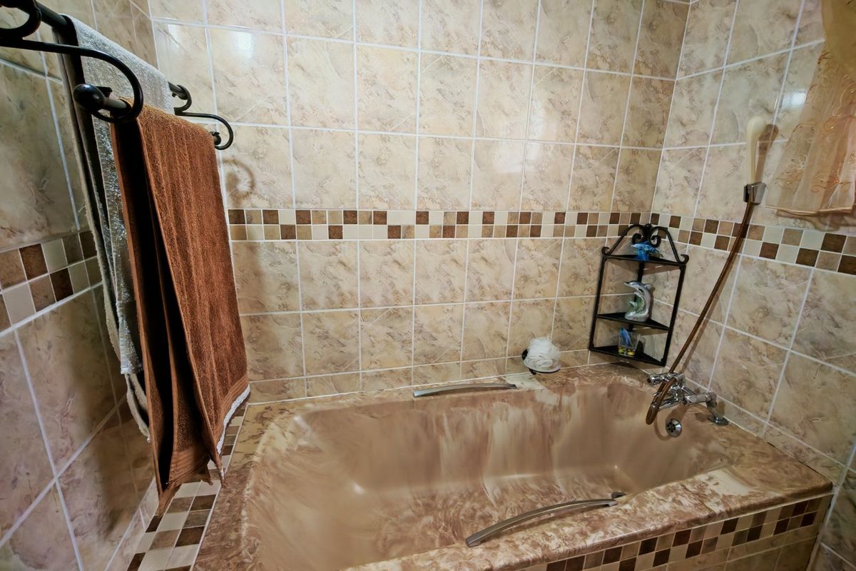 A bathroom featuring a built-in bathtub with marble-effect finish and matching wall tiles, equipped with a handheld shower head and towel rail.