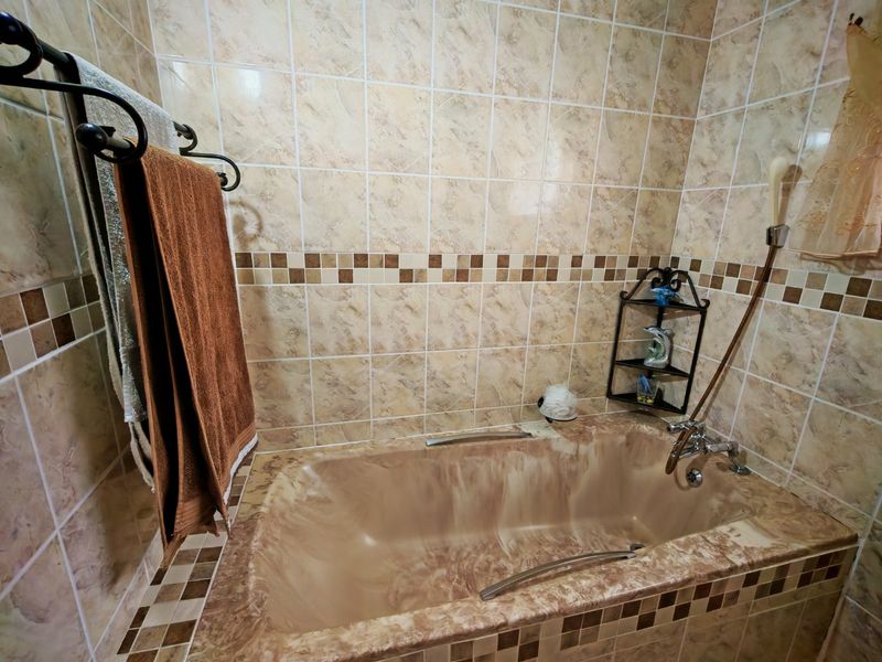 A bathroom featuring a built-in bathtub with marble-effect finish and matching wall tiles, equipped with a handheld shower head and towel rail.