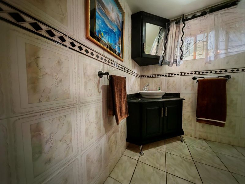 A bathroom featuring a dark vanity cabinet with a vessel sink, tiled walls with decorative borders, and tiled flooring.