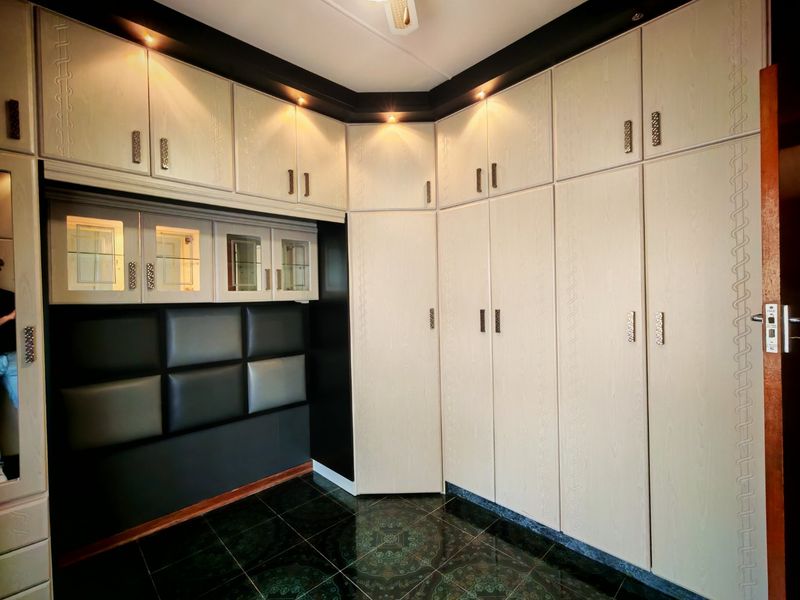 A bedroom featuring extensive built-in cabinetry with integrated lighting, glass display units, and a modern upholstered headboard panel.