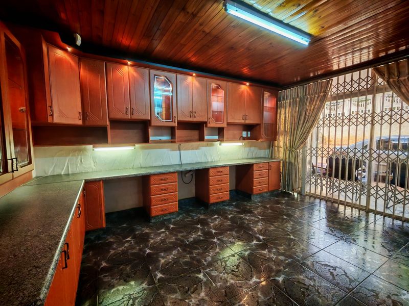 A functional scullery or utility area featuring extensive timber cabinetry, granite countertops, tiled flooring, and a timber-clad ceiling with direct access to the exterior.