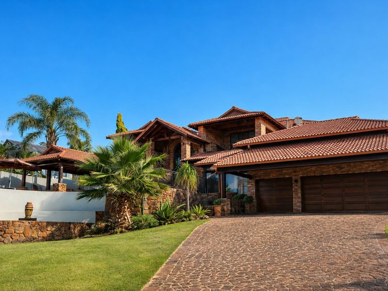 A well-maintained luxury residence featuring stone cladding, terracotta roof tiles, a double garage, and a beautifully landscaped front garden with a cobblestone driveway.