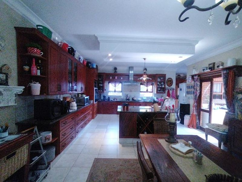 Spacious open-plan kitchen featuring extensive wooden cabinetry, granite countertops, a central island, and tiled flooring, with direct access to the outdoor area.