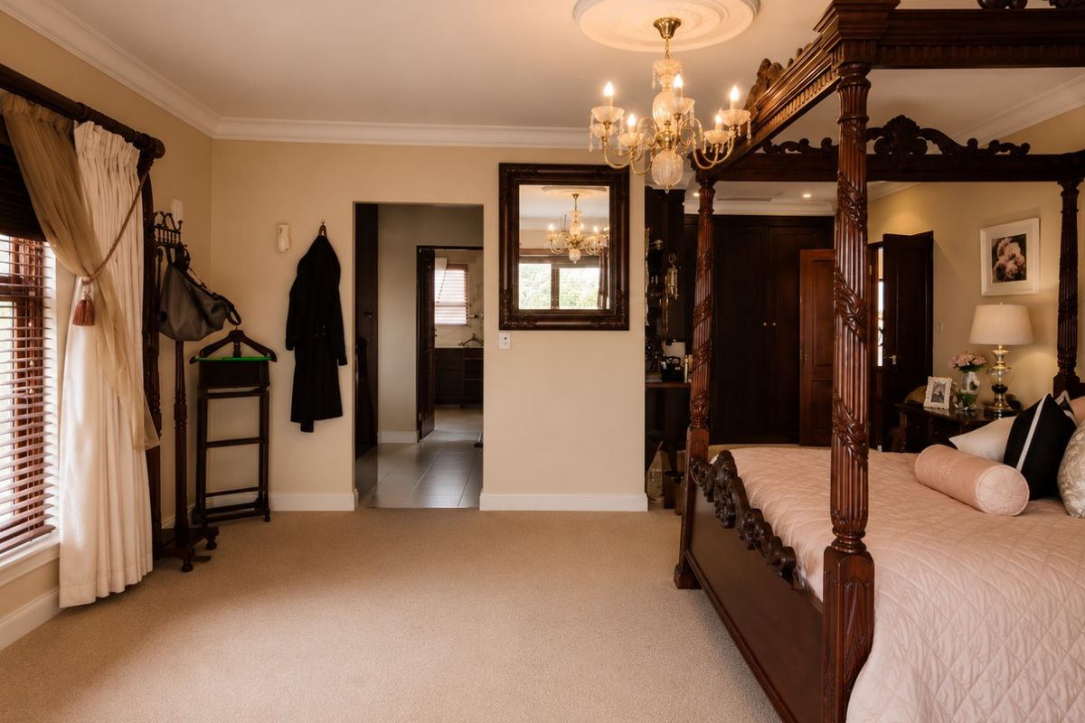 Spacious bedroom featuring a classic four-poster bed, elegant chandelier with ceiling rose, neutral carpeting, and built-in storage cabinetry.