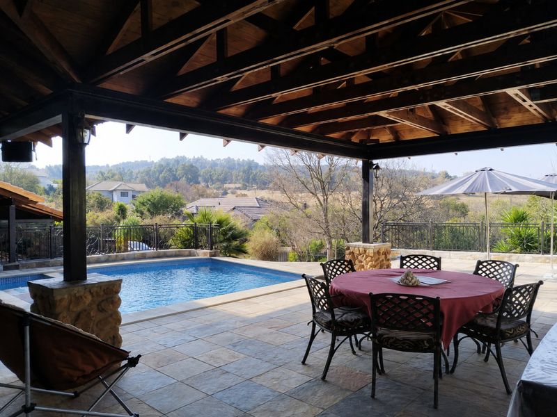 Spacious covered outdoor patio featuring a swimming pool, exposed timber ceiling, and stone-clad pillars, offering scenic views of the surrounding landscape.