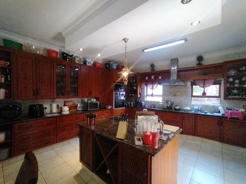 Spacious kitchen featuring extensive dark wood cabinetry, granite countertops, a central island, and integrated appliances with recessed lighting.