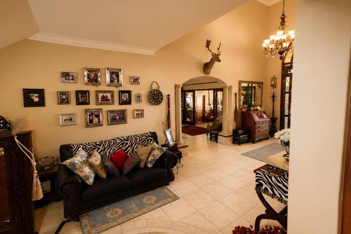 Spacious living area featuring tiled flooring, decorative columns, and an elegant archway leading to adjacent rooms, complemented by a classic chandelier.