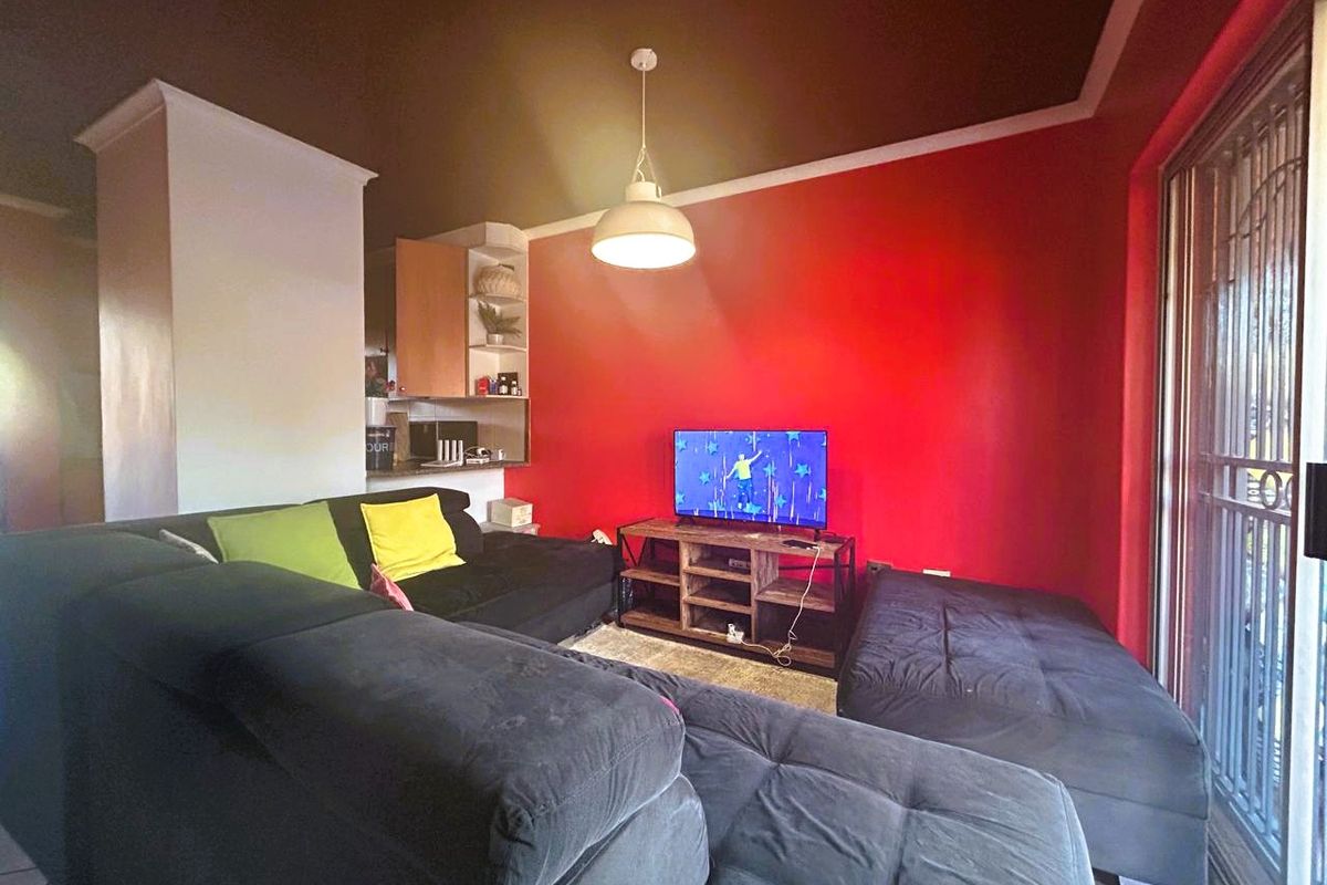 A living room featuring a bold red accent wall, pendant lighting, and a sliding glass door with security gate leading to the exterior.