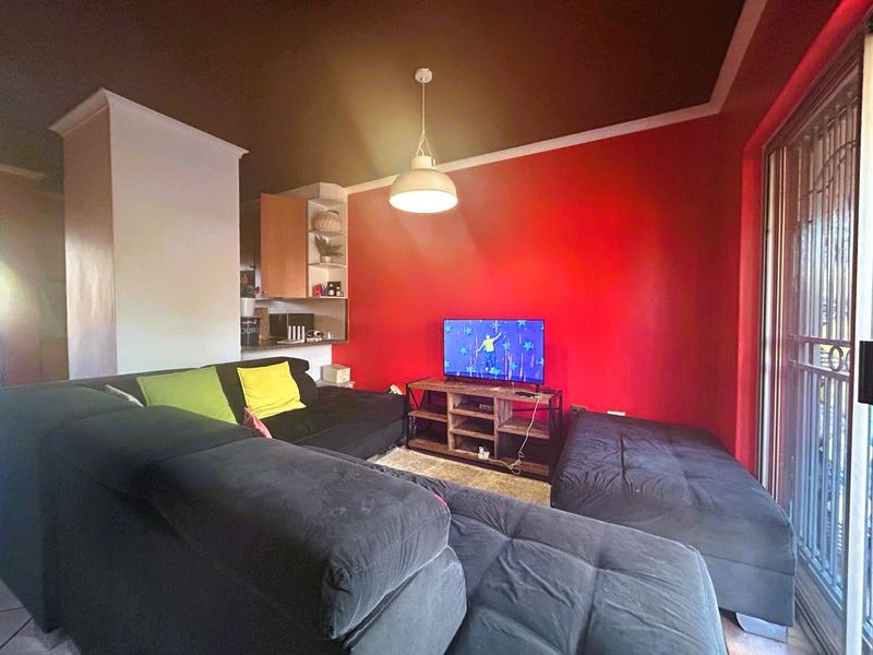 A living room featuring a bold red accent wall, pendant lighting, and a sliding glass door with security gate leading to the exterior.