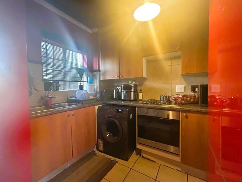 Compact kitchen featuring wooden cabinetry, built-in oven, gas hob, stainless steel sink, and tiled flooring with a functional layout.