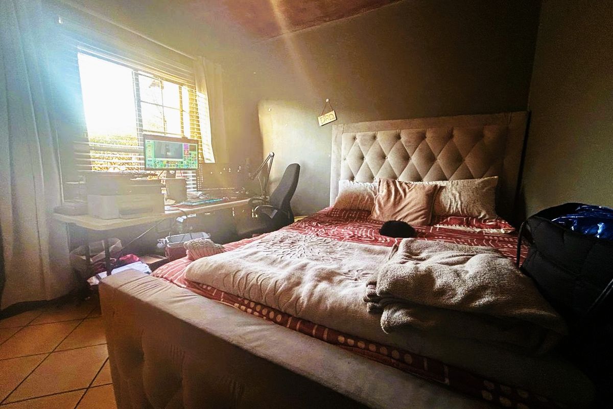 A bedroom featuring tiled flooring and a window with blinds, currently showing signs of wear on the ceiling and wall finishes.