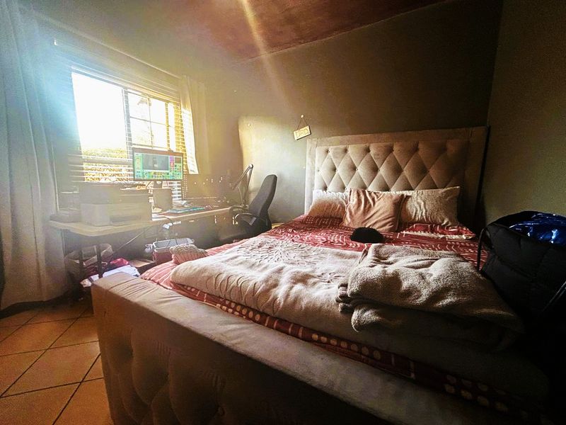 A bedroom featuring tiled flooring and a window with blinds, currently showing signs of wear on the ceiling and wall finishes.