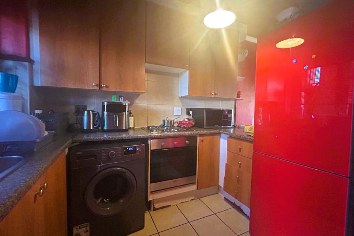 Compact kitchen featuring laminate cabinetry, granite countertops, built-in oven, electric hob, and tiled flooring.