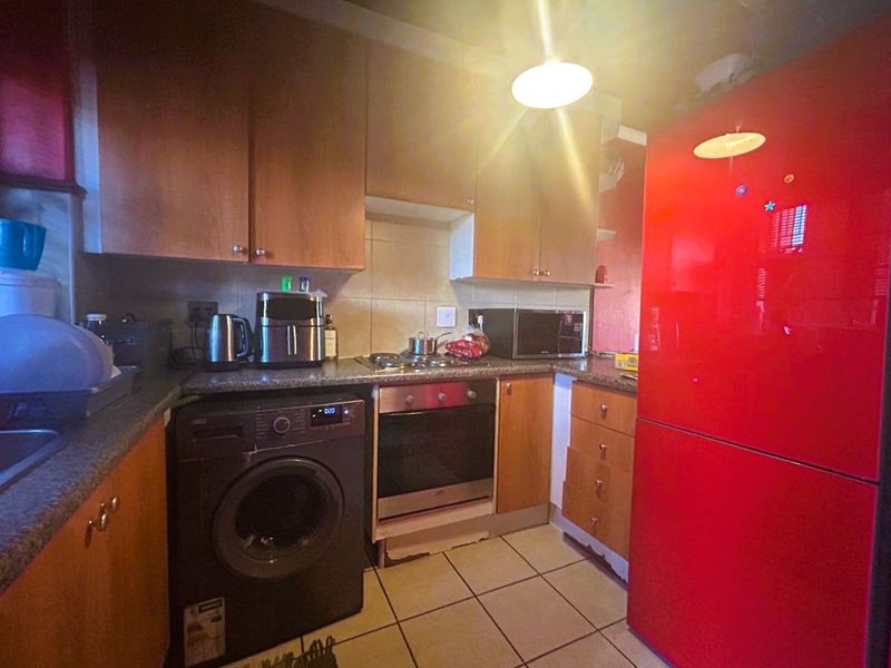 Compact kitchen featuring laminate cabinetry, granite countertops, built-in oven, electric hob, and tiled flooring.