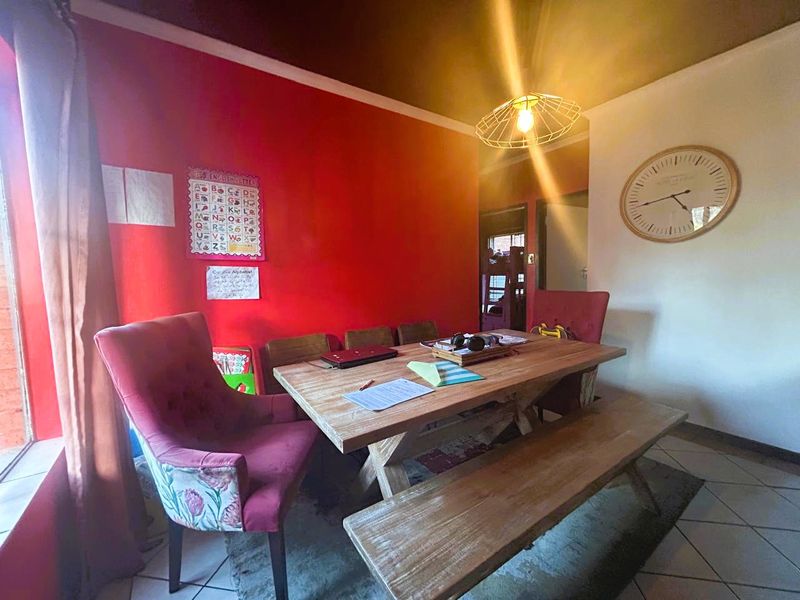 A dining room featuring tiled flooring and a central pendant light fixture, currently utilized as a multi-purpose space.