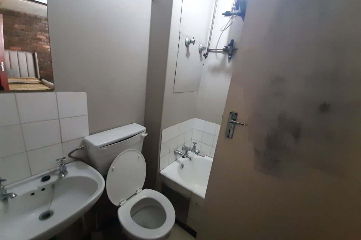 A compact bathroom featuring a pedestal basin, toilet, and bathtub with dated fixtures and exposed plumbing, requiring cosmetic updates.