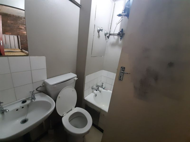 A compact bathroom featuring a pedestal basin, toilet, and bathtub with dated fixtures and exposed plumbing, requiring cosmetic updates.