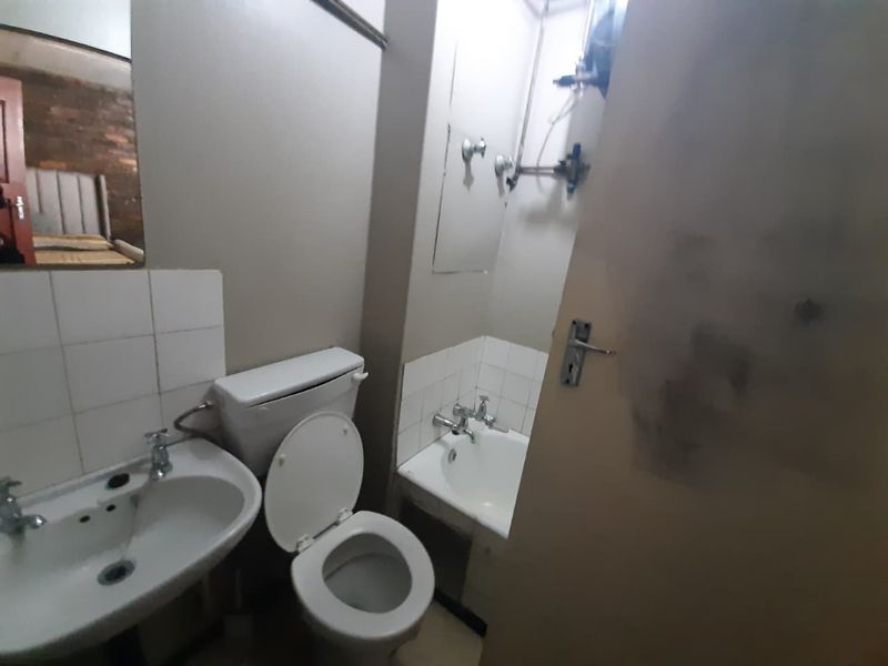 A compact bathroom featuring a pedestal basin, toilet, and bathtub with exposed plumbing, requiring cosmetic updates to improve the overall finish.