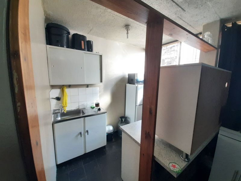 A compact kitchen area featuring basic cabinetry, a stainless steel sink, and a tiled splashback, currently showing signs of age and wear.