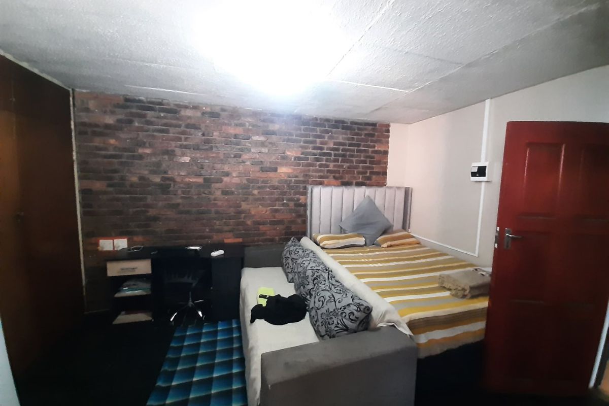 A bedroom featuring an exposed brick accent wall, built-in storage, and a textured ceiling finish, offering potential for cosmetic updates.