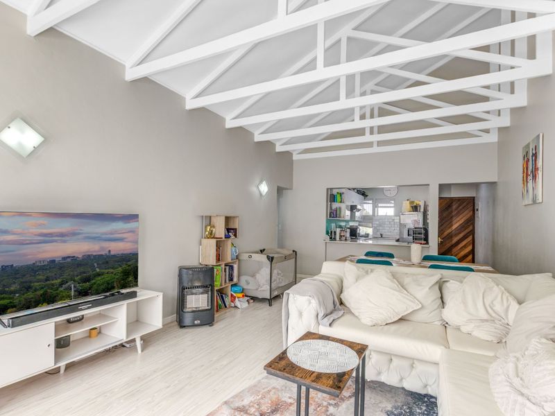 Spacious open-plan living area featuring high vaulted ceilings with exposed white trusses and light laminate flooring, seamlessly connecting to the kitchen.