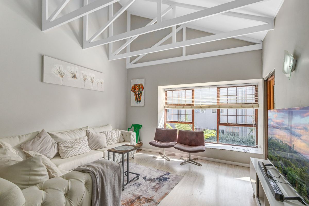 Bright living room featuring high vaulted ceilings with exposed white trusses, laminate flooring, and a large window providing natural light.