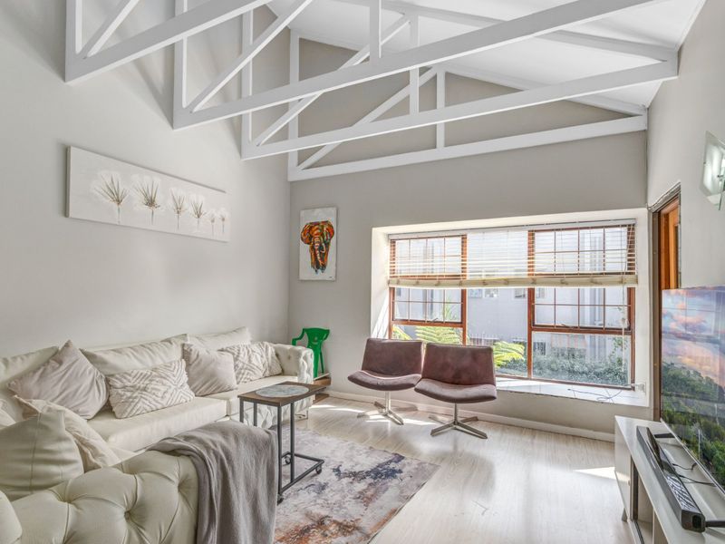 Bright living room featuring high vaulted ceilings with exposed white trusses, laminate flooring, and a large window providing natural light.