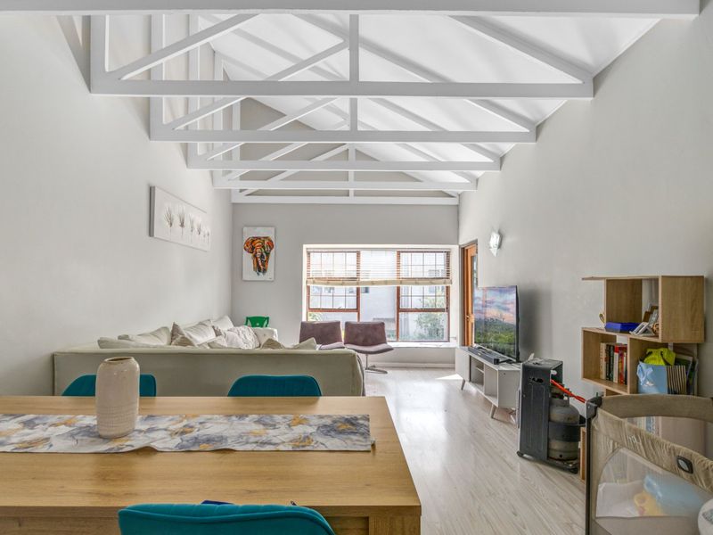 Spacious open-plan living area featuring high vaulted ceilings with exposed white trusses and bright laminate flooring, creating an airy and inviting atmosphere.