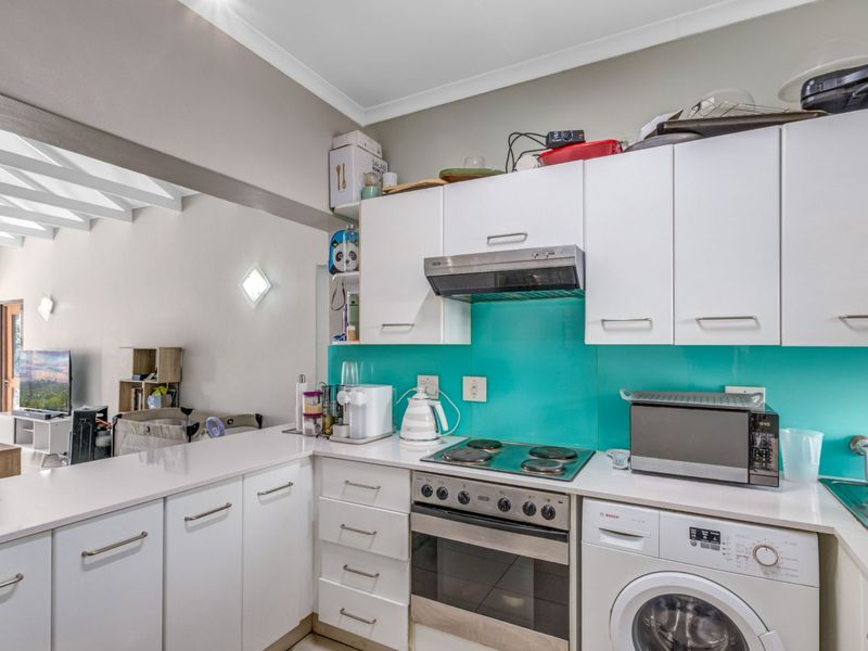 Compact kitchen featuring white cabinetry, quartz countertops, a vibrant glass splashback, and integrated appliances including an oven, hob, and washing machine.