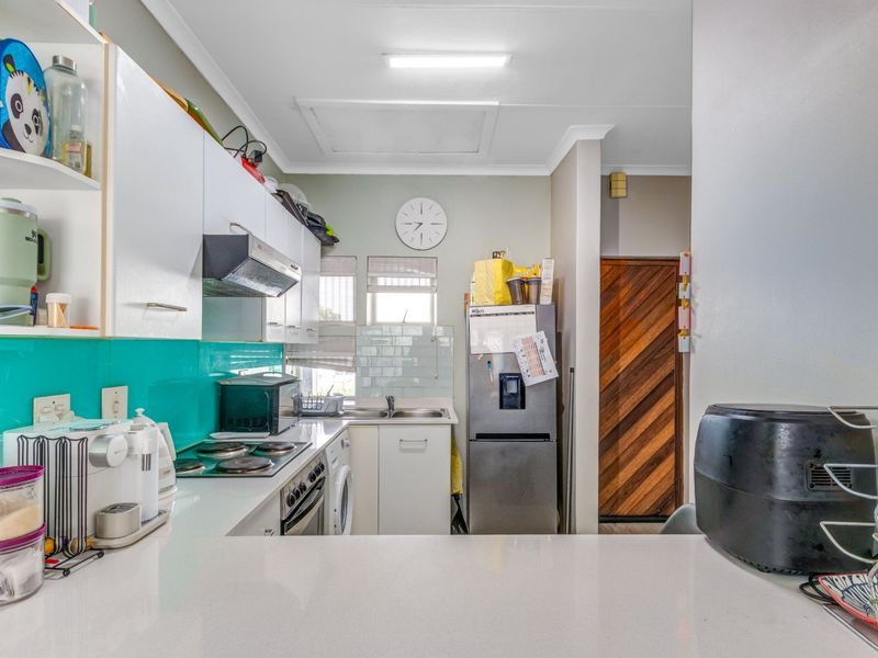 Functional kitchen featuring white cabinetry, stone countertops, electric hob, extractor fan, and a tiled splashback, providing a practical workspace for daily cooking.