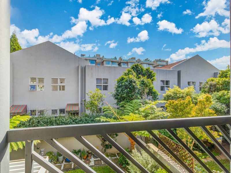 A view from a balcony overlooking a lush garden area and neighboring apartment complex buildings.