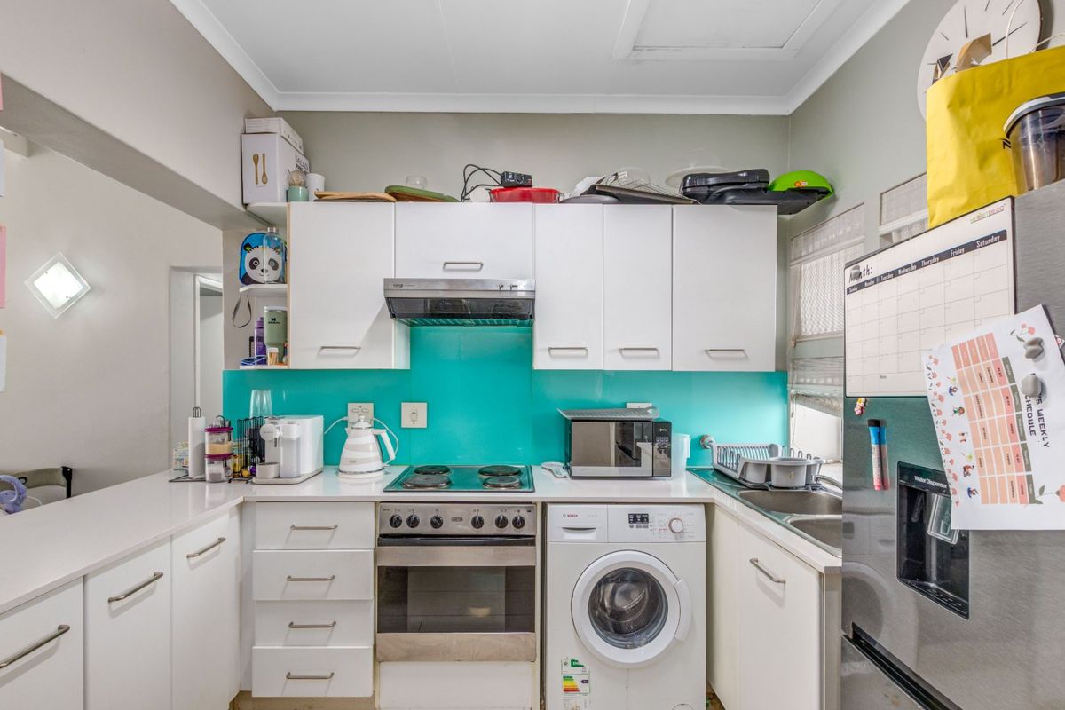 Compact kitchen featuring white cabinetry, a vibrant turquoise glass splashback, integrated washing machine, and built-in electric oven with cooktop.