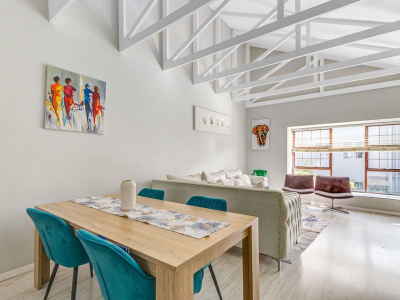 Bright open-plan living and dining area featuring high vaulted ceilings with exposed white trusses and light-toned laminate flooring.