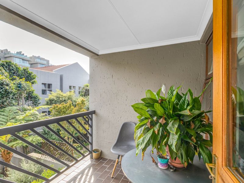 A covered balcony featuring tiled flooring and a metal balustrade, offering a pleasant outdoor space with views of the surrounding greenery.