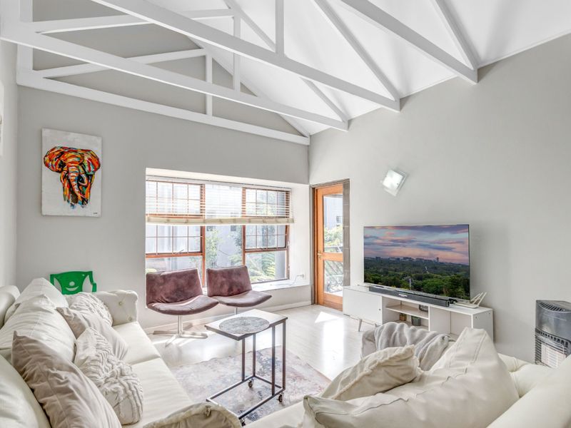 A bright living room featuring a high vaulted ceiling with exposed white trusses, large windows, and a timber-framed exterior door.
