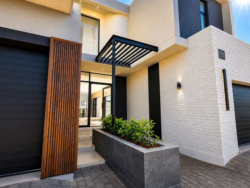 Modern architectural front facade featuring a double garage, timber slat accents, painted brickwork, and a contemporary pergola entrance with a built-in planter.