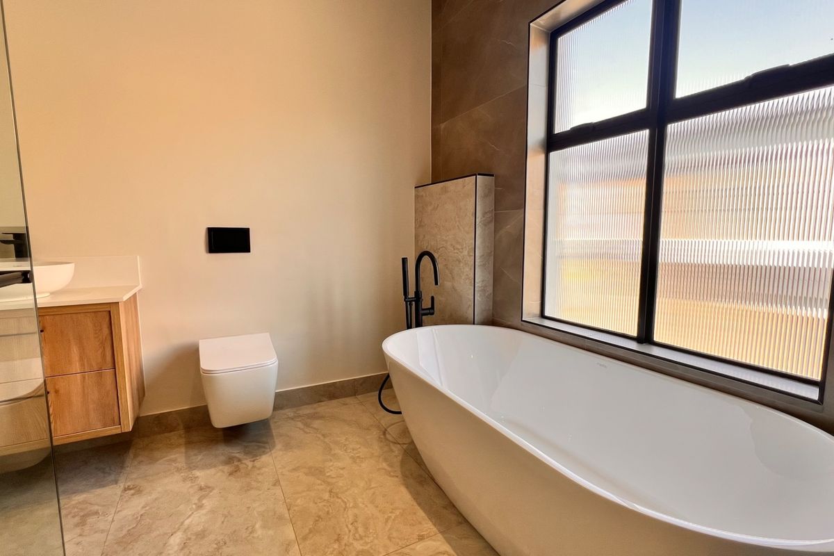 Modern bathroom featuring a sleek freestanding bathtub, wall-mounted toilet, and a contemporary vanity with a vessel sink and matte black fixtures.