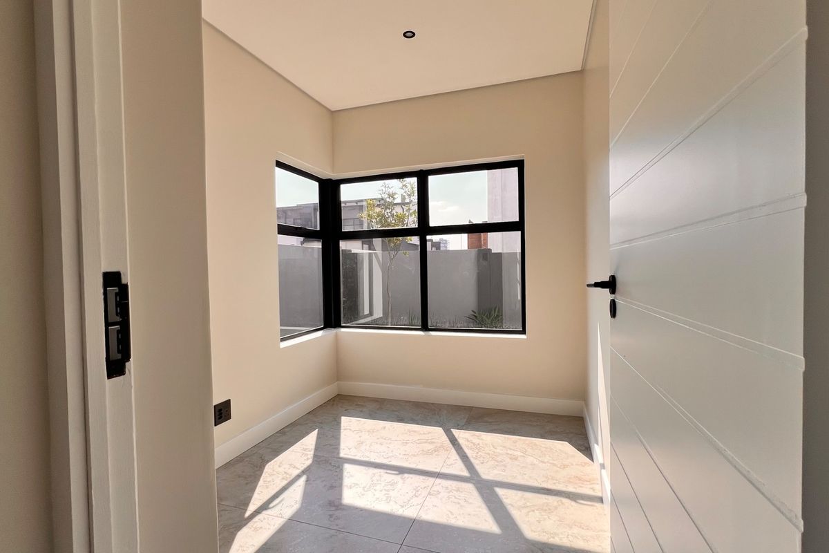 A bright, empty bedroom featuring modern tiled flooring, clean neutral walls, and a large black-framed corner window providing natural light.