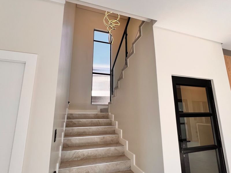A modern, well-lit hallway featuring a stone-tread staircase with a black metal handrail, a tall vertical window, and a contemporary pendant light fixture.