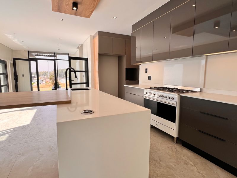 Modern kitchen featuring high-gloss cabinetry, a central island with quartz countertops, integrated gas stove, and sleek tiled flooring in an open-plan layout.