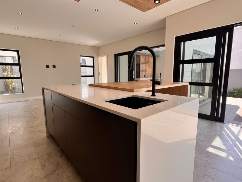 Modern open-plan kitchen area featuring a large central island with stone countertops, black fixtures, and seamless access to the outdoor pool area.