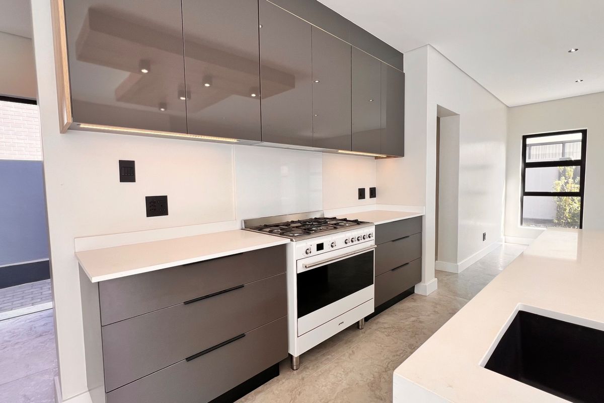 Modern kitchen featuring sleek gloss cabinetry, quartz countertops, a gas cooktop with oven, and integrated lighting, offering a clean and contemporary culinary space.