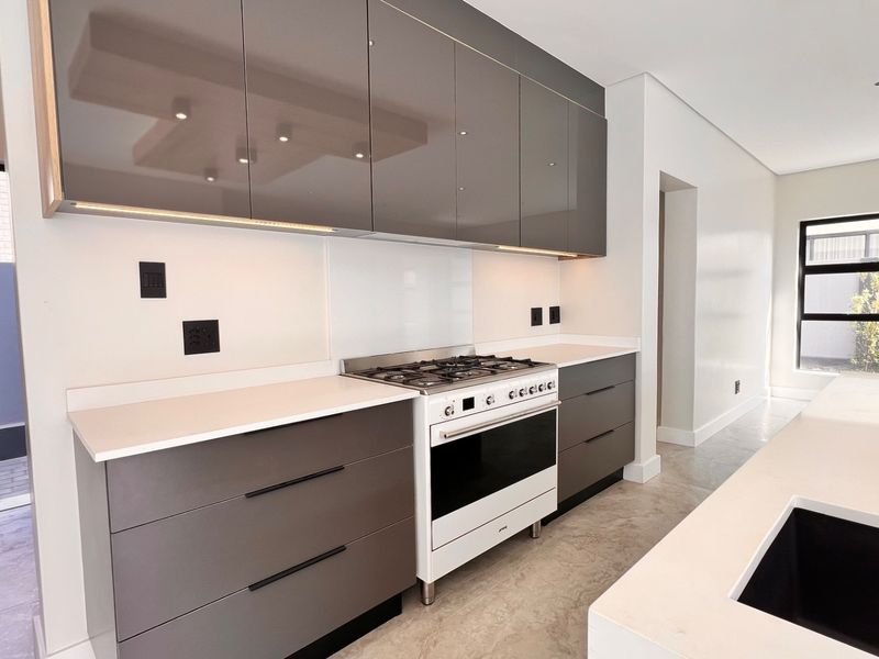 Modern kitchen featuring sleek gloss cabinetry, quartz countertops, a gas cooktop with oven, and integrated lighting, offering a clean and contemporary culinary space.
