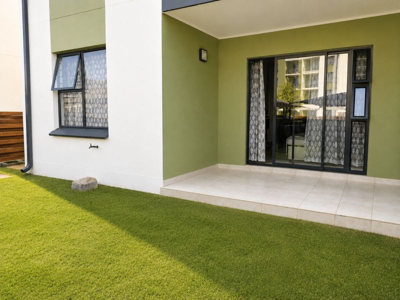 A clean, tiled patio area featuring sliding glass doors, modern casement windows, and an external water tap, overlooking a well-maintained lawn.