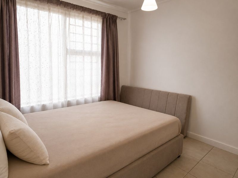 A neutrally decorated bedroom featuring tiled flooring and a large window with curtain fixtures.